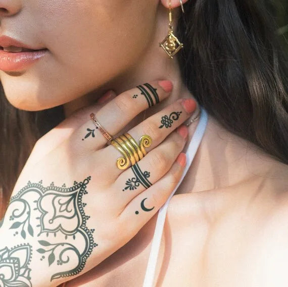Plan rapproché d'une main féminine ornée de tatouage au henné, avec des bagues élégantes et une boucle d'oreille, évoquant une esthétique délicate et moderne.